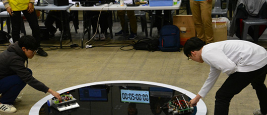 두 명의 참가자가 각 로봇을 경기장에 놓고 배틀을 시작하는 사진